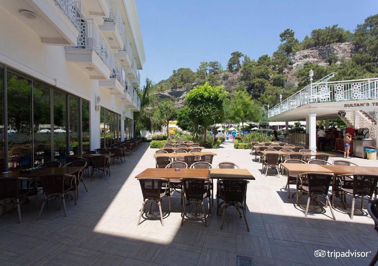 Miramor Hotel & Spa アンタルヤ エクステリア 写真 The photo shows an outdoor dining area, likely at a restaurant or cafe. There are several tables with chairs arranged neatly on the paved ground, and some greenery, such as trees and plants, is visible in the background. The setting appears bright an